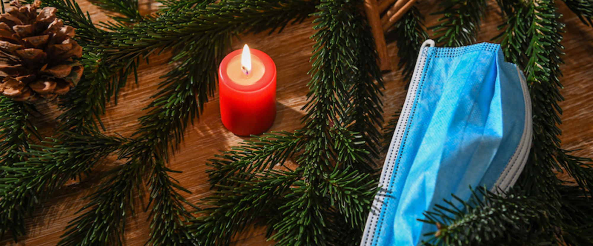 Eine Maske liegt in einer weihnachtlichen Dekoration aus Tannenzweigen und Tannenzapfen am 5. Dezember 2020 in Bonn. In der Mitte brennt eine rote Kerze.