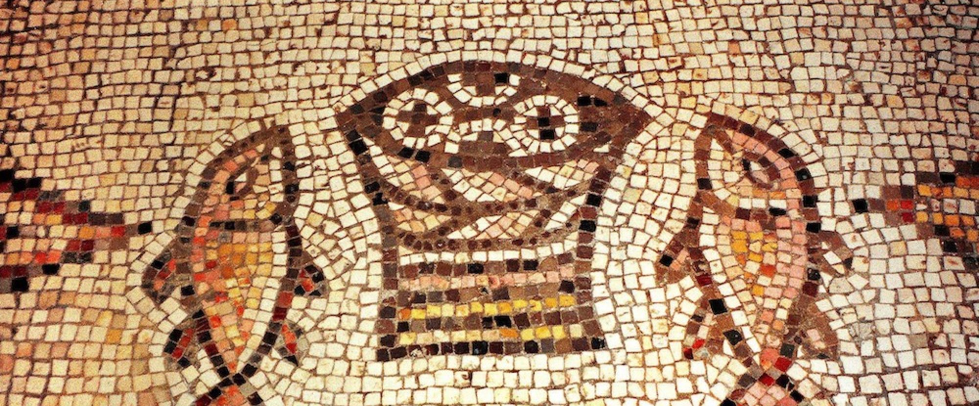 Das berühmte Brot- und Fisch-Mosaik in der Brotvermehrungskirche Tabgha am See Genezareth in Israel: Aus einem Korb ragen vier runde, mit Kreuzen gezeichnete Brote hervor. Links und rechts davon liegt ein Fisch, der gedrungenen Form nach wohl ein Pet