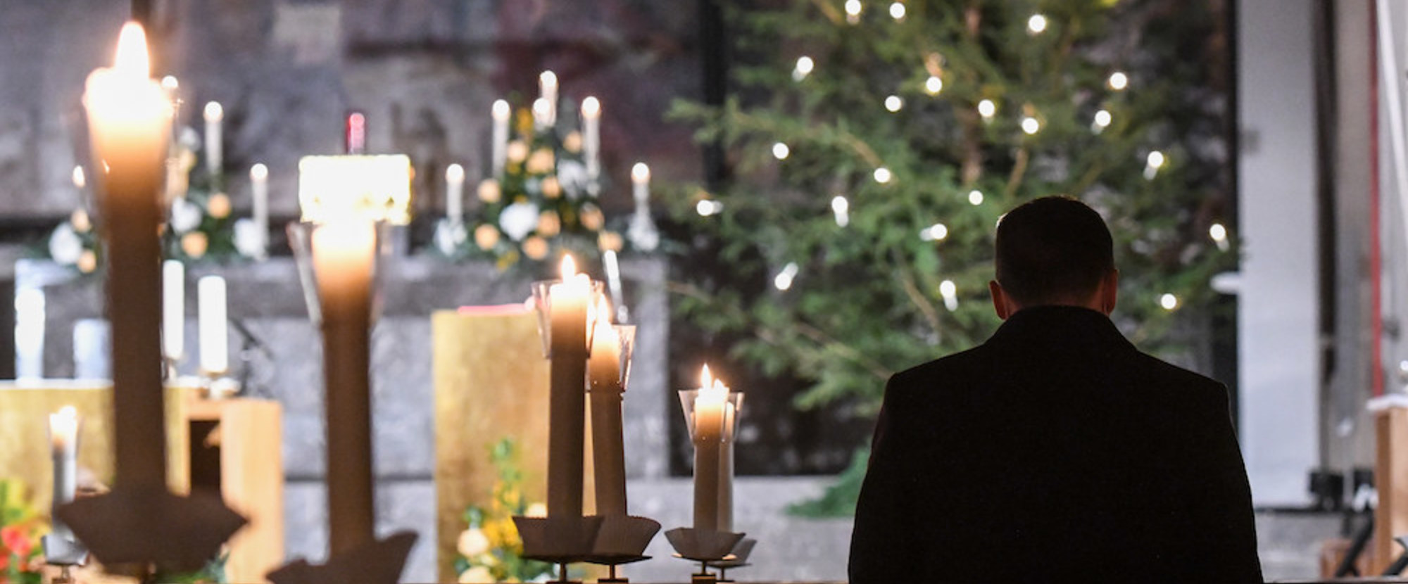 Ein Mann kniet neben Kerzen vor einer Christmette in der Kirche Sankt Remigius in Bonn am 24. Dezember 2020.