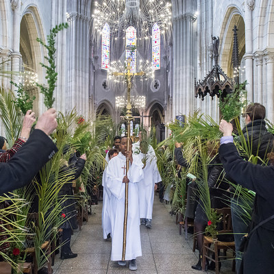 Messdiener laufen durch den mit Palmblättern geschmückten Mittelgang der Kirche Saint-Jean-Baptiste de Belleville in Paris nach dem Palmsonntagsgottesdienst am 25. März 2018. Menschen halten Palmzweige in die Höhe, ein Ministrant trägt ein goldenes K