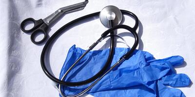 blaue OP-Handschuhe, Stethoskop, Verbandsschere auf weißem Tischtuch liegend