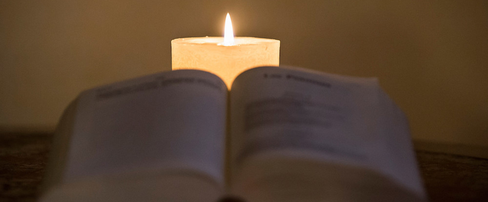 Eine Bibel liegt aufgeschlagen auf einem Tisch, dahinter brennt eine weiße Kerze am 3. Januar 2020. (Aufnahmeort unbekannt)