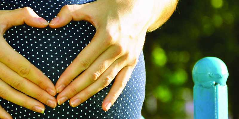 Hände formen ein Herz auf dem Bauch einer schwangeren Frau.