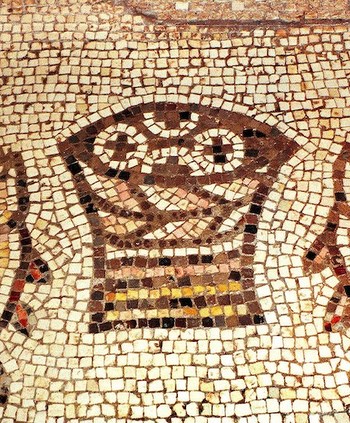 Das berühmte Brot- und Fisch-Mosaik in der Brotvermehrungskirche Tabgha am See Genezareth in Israel: Aus einem Korb ragen vier runde, mit Kreuzen gezeichnete Brote hervor. Links und rechts davon liegt ein Fisch, der gedrungenen Form nach wohl ein Pet