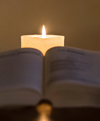 Eine Bibel liegt aufgeschlagen auf einem Tisch, dahinter brennt eine weiße Kerze am 3. Januar 2020. (Aufnahmeort unbekannt)